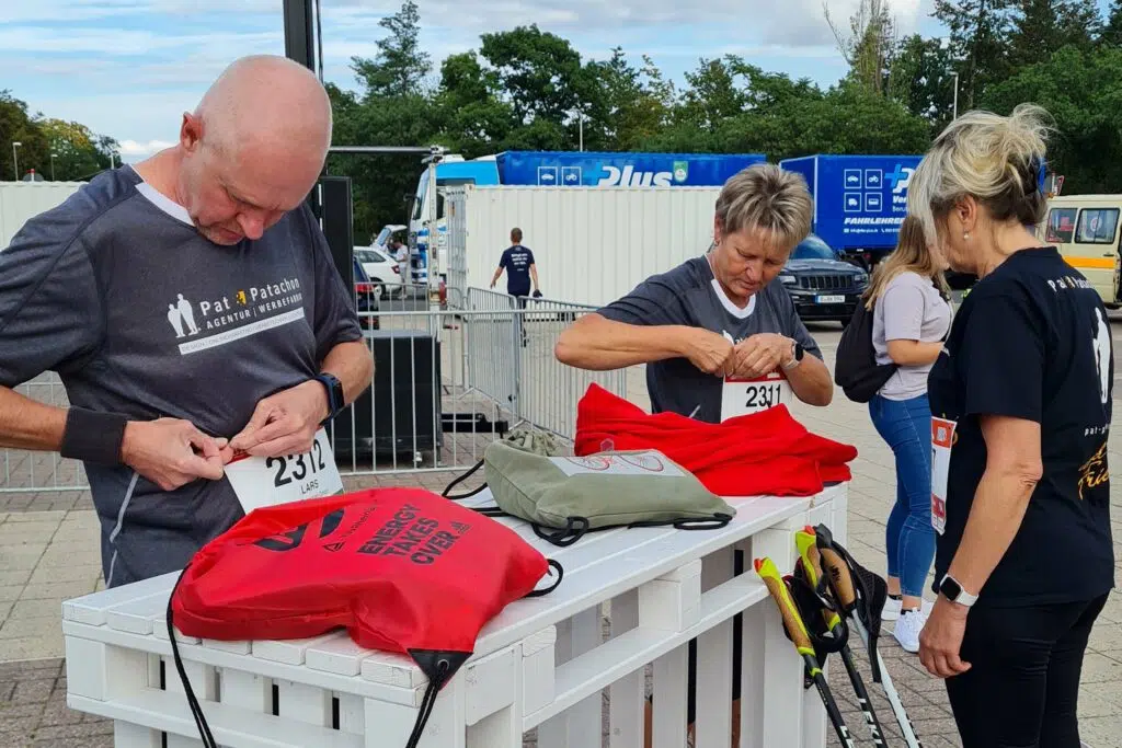 Teammitglieder von Pat & Patachon bereiten sich auf den B2Run vor. Mit voller Konzentration befestigen sie ihre Startnummern, während Nordic-Walking-Stöcke und Sportbeutel bereitstehen. Die Vorfreude auf das sportliche Event ist deutlich spürbar.