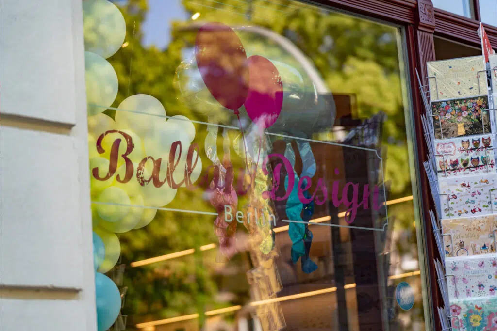 Ein schönes Detailfoto der Schaufensterbeschriftung von „Ballon Design Berlin“! Die verspielte Typografie mit den Ballon-Grafiken spiegelt perfekt die festliche und kreative Atmosphäre des Geschäfts wider. Die Reflexionen im Glas verleihen dem Bild eine lebendige Tiefe.