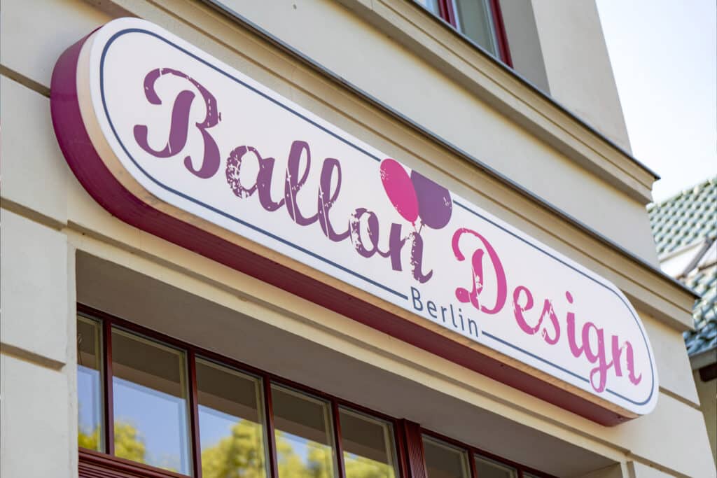 Ein charmantes und einladendes Schild für „Ballon Design Berlin“! Die verspielte Schriftart und die harmonische Farbgebung in Lila- und Pinktönen spiegeln Kreativität und Leichtigkeit wider – perfekt für einen Shop, der mit Ballons besondere Momente gestaltet.