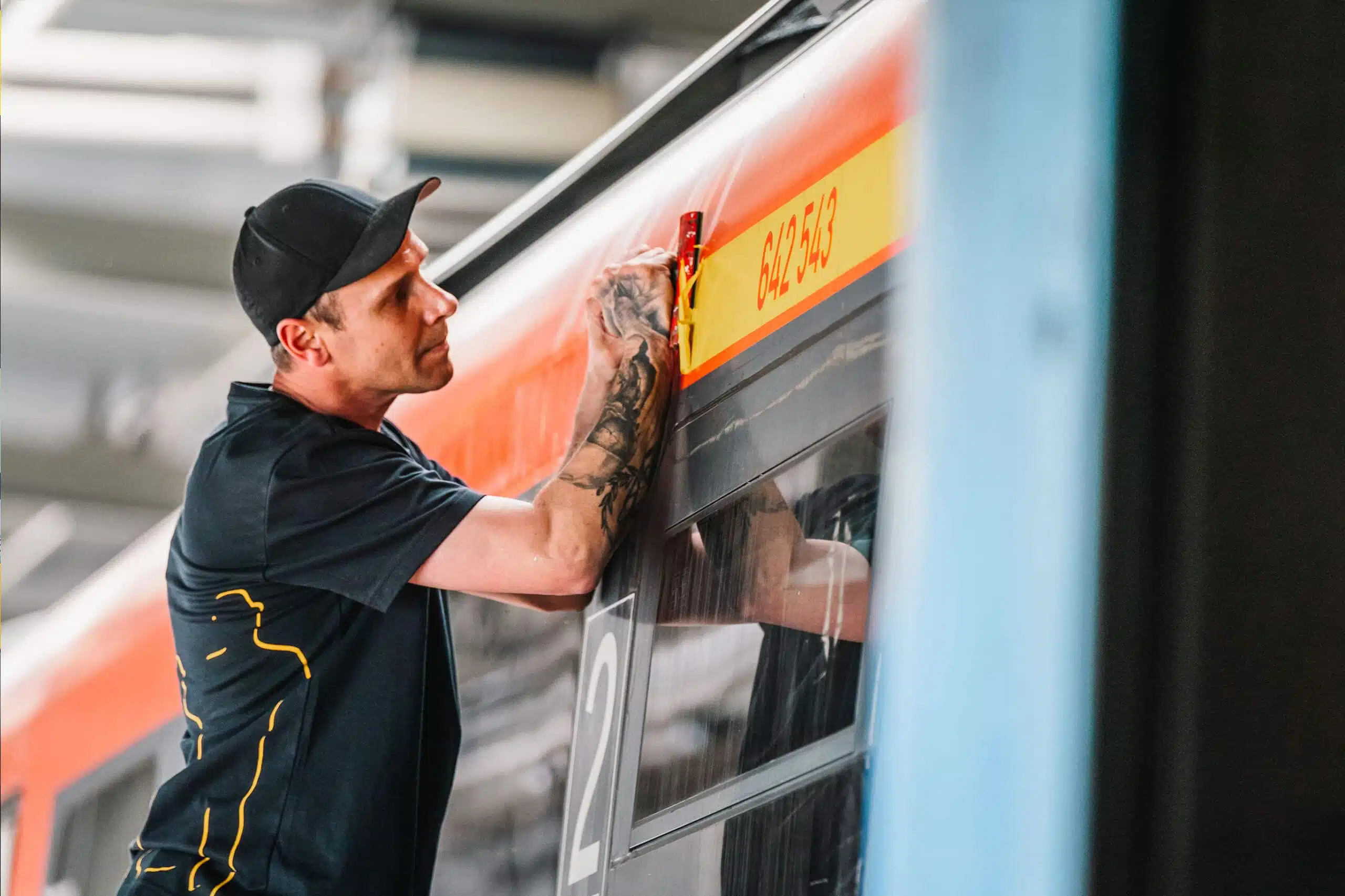 Ein Mitarbeiter entfernt mit großer Präzision eine Fahrzeugnummer auf einem Zug. Seine konzentrierte Haltung unterstreicht sein handwerkliches Können.
