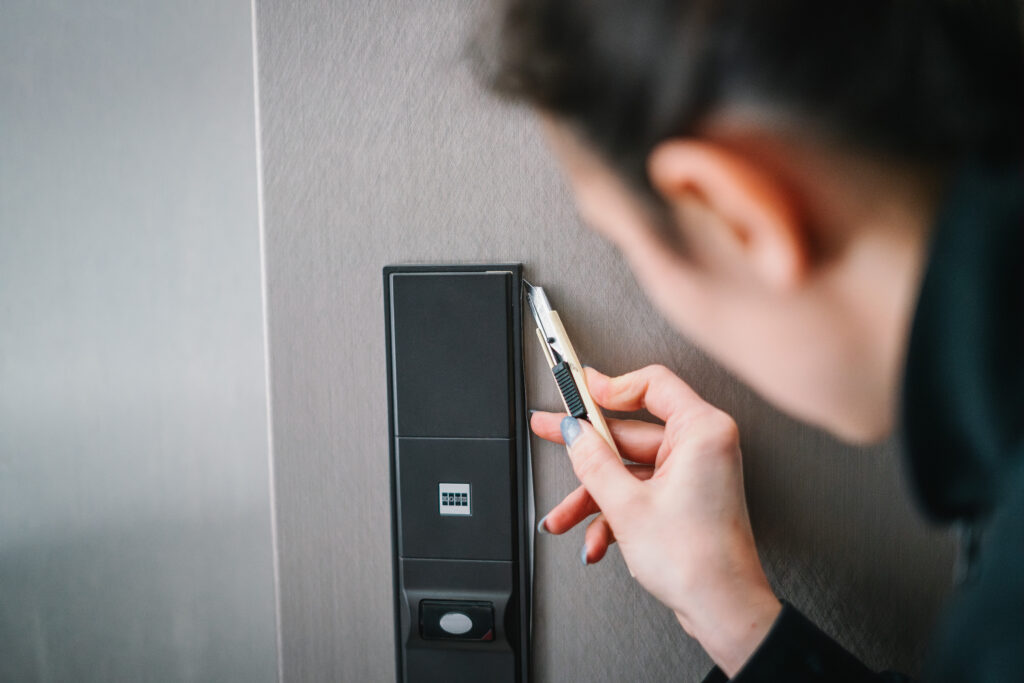 Eine Werbetechnikerin schneidet mit einem Cutter-Messer sorgfältig eine hochwertige Möbelfolie um ein Bedienelement eines Aufzugs zurecht. Die Folie in edler Metall-Optik sorgt für eine elegante, moderne Veredelung der Oberfläche.